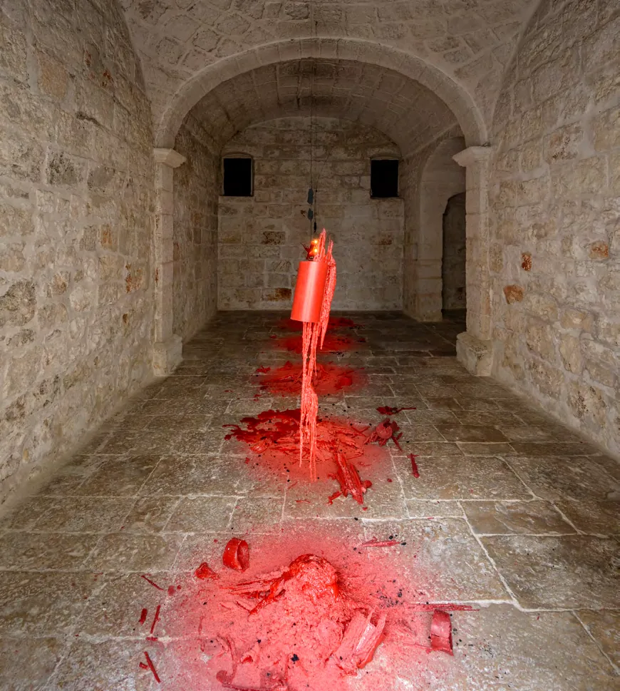 Red wax burning and dripping from a suspended vessel onto the stone floor of a vaulted chapel