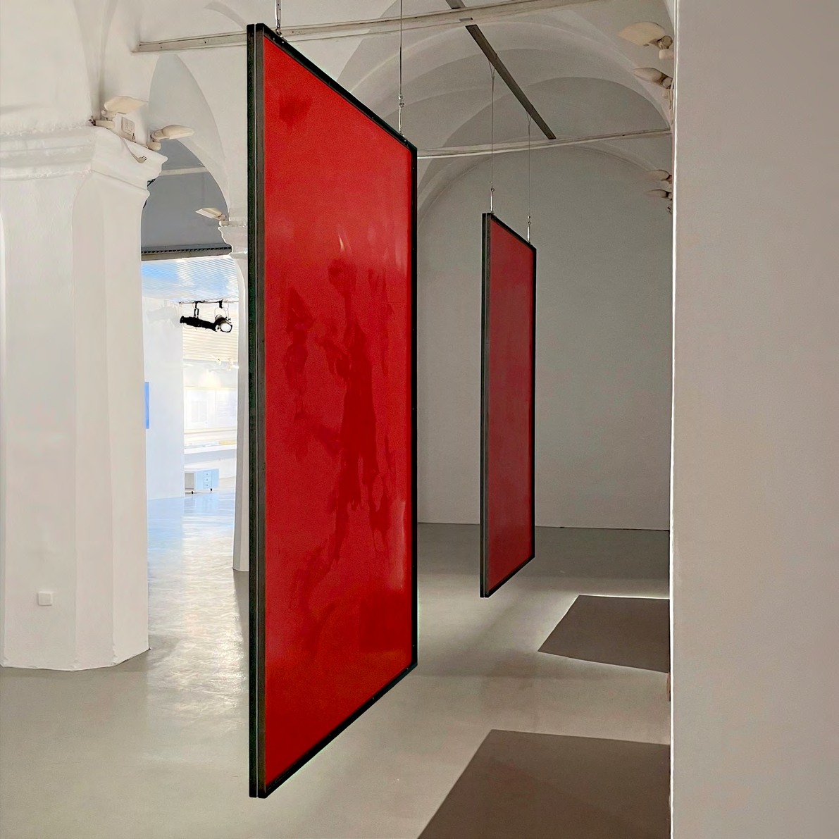 Two suspended red translucent portrait works installed in a vaulted gallery